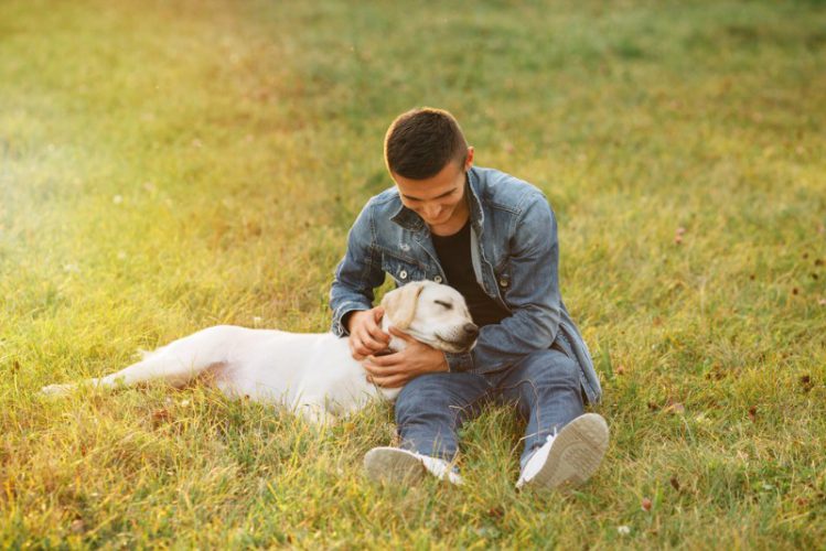 草むらの上で抱きしめ合う飼い主と犬